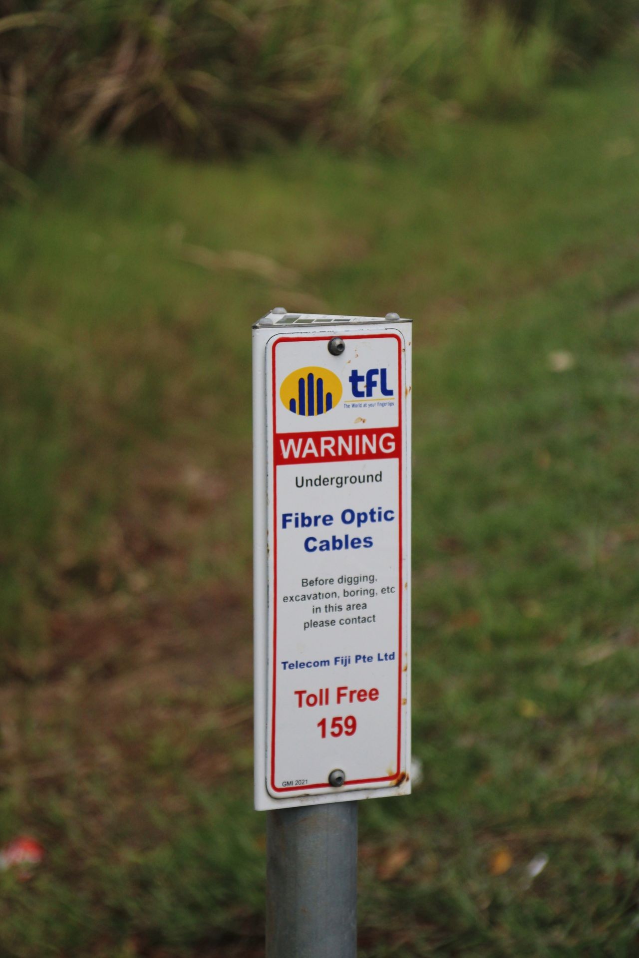 Warning sign for underground fibre optic cables at a grassy roadside, Telecom Fiji contact information included.