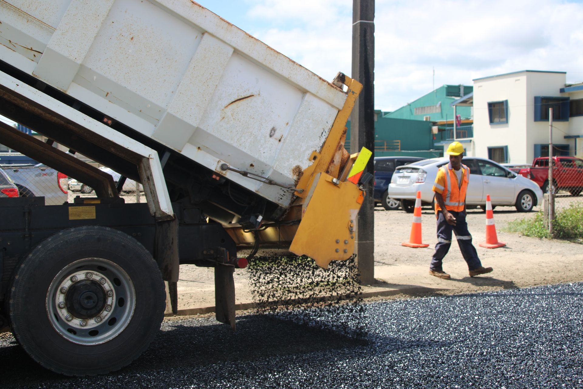 Dump truck laying asphalt on a road with a construction worker nearby in safety gear.