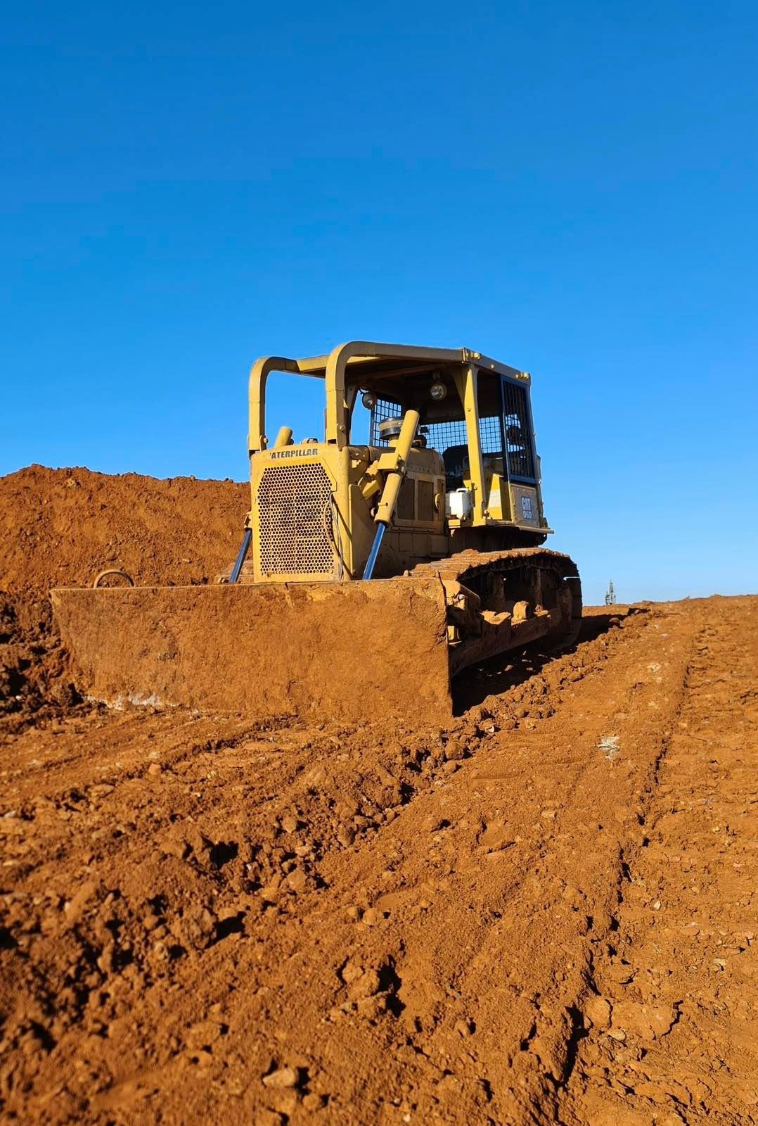 Yellow bulldozer moving dirt on a construction site under a clear blue sky.